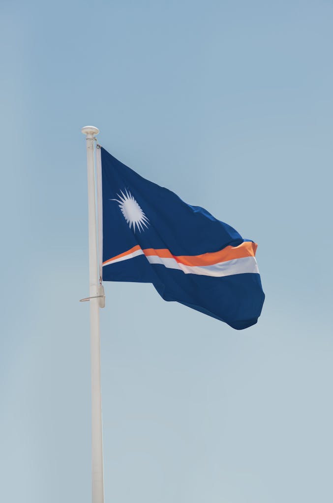 Marshall Islands national flag waving on a flagpole against a clear sky, symbolizing patriotism.